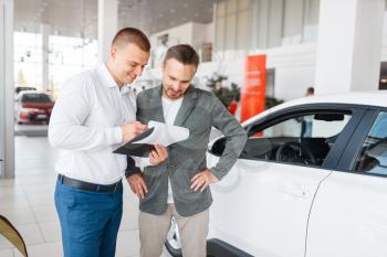 Salesman and buyer make out the purchase of new car in showroom. Male customer buying vehicle in dealership, automobile sale