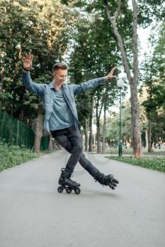 Roller skating, male teenager rolling on one leg in park. Urban roller-skating, active extreme sport
