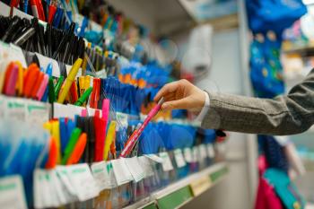 School girl choosing a pen at the shelf in stationery store. Female child buying office supplies in shop, schoolchild in supermarket