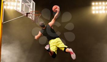 Basketball player makes shoot in jump, dark background. Male athlete in sportswear scores on streetball training