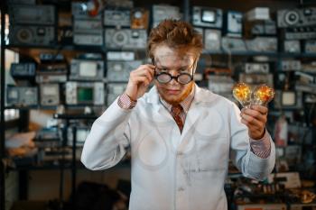 Strange engineer holds electric lamp in laboratory. Electrical testing tools on background. Lab equipment, engineering workshop