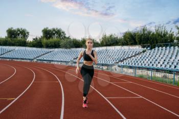 Female jogger in sportswear running, training on stadium. Woman doing stretching exercise before jogging on outdoor arena