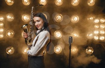 Female saxophonist poses with saxophone on the stage with spotlights. Jazz performer playing on the scene