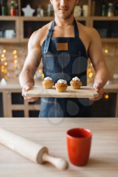 Naked man in apron holds tray with sweet dessert on the kitchen. Nude male person preparing breakfast at home, food preparation without clothes