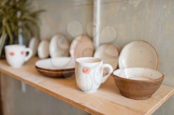 Kitchen utensils on shelf in pottery workshop, nobody. Handmade clay tableware molding and shaping