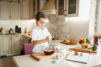 Young boy mixing melted chocolate in a bowl. Cute male kid cooking on the kitchen. Happy child prepares sweet dessert at the counter