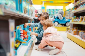 Little boy and girl at the shelf in kids store, side view. Brother and sister choosing toys in supermarket, family shopping, young customers