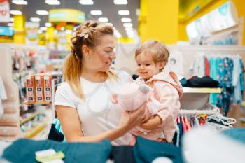 Mother with her little daughter choosing plush dog in kids store. Mom and child buying toys in supermarket together, family shopping
