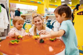 Mother with her little children playing in kids store. Happy mom with daughter and son buying toys in supermarket together, family shopping