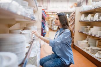 Young woman choosing plates in houseware store. Female person buying home goods in market, lady in kitchenware supply shop