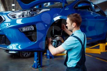 Worker in uniform fix problem on vehicle with removed wheel, car service station. Automobile checking and inspection, professional diagnostics and repair