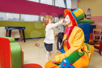 Funny clown play with little girl in kindergarten. Birthday celebrating in playroom, baby holiday in playground. Childhood happiness, childish leisure