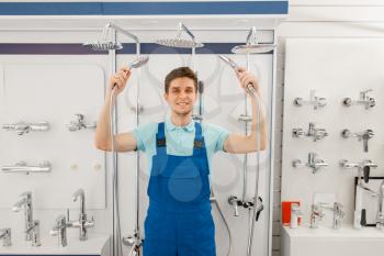 Plumber in uniform choosing shower at showcase in plumbering store. Man buying sanitary engineering in shop, bathroom equipment choice