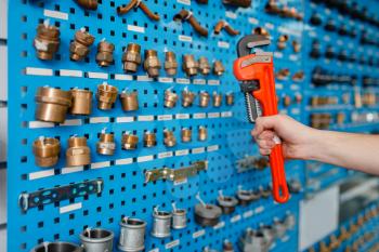 Plumber hand holds pipe wrench at the showcase in plumbering store. Man buying sanitary engineering in shop