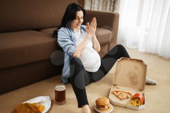 Pregnant woman with belly smoking and eats unhealthy food at home. Pregnancy, bad habits and lifestyle in prenatal period. Ugly expectant mom, health damage