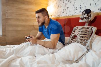 Man playing game console, wife skeleton in the bed, bad relationship. Couple having a problems, family quarrel or conflict