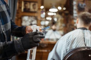 Barber processes the blade with spray, customer sitting in chair. Professional barbershop is a trendy occupation. Male hairdresser and client in hair salon
