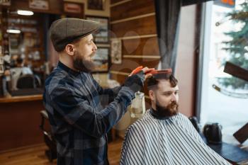Barber with comb and electric clipper makes a haircut to a client. Professional barbershop is a trendy occupation. Male hairdresser and customer in retro style hair salon