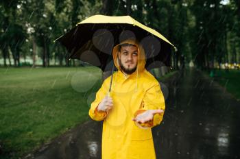 Man with umbrella walking in summer park in rainy day. Male person in rain cape and rubber boots, wet weather