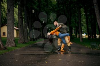 Happy love couple dancing in park in summer rainy day. Man and woman hugs under umbrella in rain, romantic date on walking path, wet weather in alley