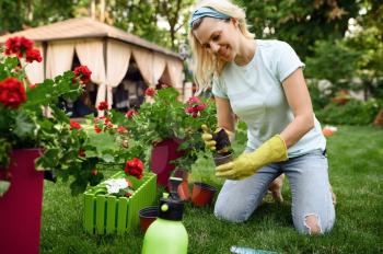 Smiling woman transplants flowers in the garden. Female gardener takes care of plants outdoor, gardening hobby, florist lifestyle and leisure