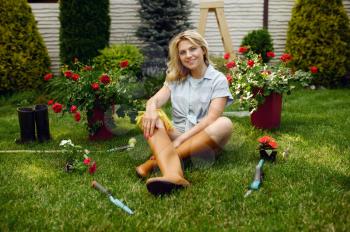 Happy female gardener sitting on the grass in the garden. Woman takes care of plants outdoor, gardening hobby, florist lifestyle and leisure