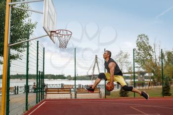 Basketball player makes a throw, shoot in jump, outdoor court. Male athlete in sportswear scores on streetball training