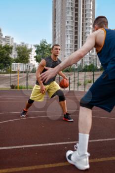 Two basketball players work out tactics on outdoor court. Male athletes in sportswear play the game on streetball training