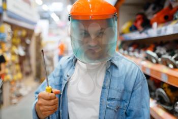 Male buyer in the mask holds screwdriver, hardware store. Customer look at the goods in diy shop, shopping in building supermarket