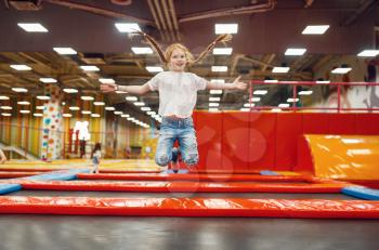 Jouful girl jumping on a trampoline in the entertainment center. Female child leisures on holidays, childhood happiness, happy kids on playground