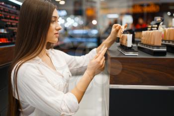 Beautiful woman at the shelf in cosmetics store, side view. Buyer at the showcase in luxury beauty shop salon, female customer in fashion market