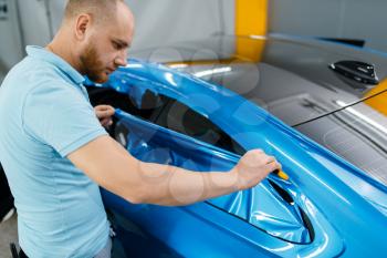 Car wrapping, mechanic cuts protective vinyl foil or film on vehicle. Worker makes auto detailing. Automobile paint protection coating, professional tuning