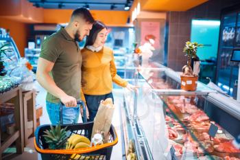 Family couple choosing fresh chilled meat in grocery store. Man and woman with cart buying beverages and products in market, customers shopping food and drinks