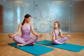 Mother and daughter doing relaxation exercise on mats in gym, yoga workout. Mom and little girl in sportswear, joint training in sport club
