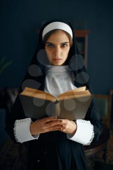 Young nun in a cassock reads a prayer, front view. The sister in the monastery, religion and faith, religious people