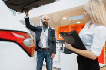 Man and female seller looking auto in car dealership. Customer and saleswoman in vehicle showroom, male person buying transport, automobile dealer business