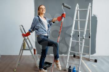 Female house painter with paint roller sitting on a ladder. Home repair, happy woman doing appartment renovation