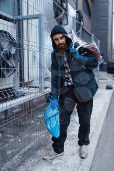Male bearded beggar with bag on city street. Poverty is a social problem, homelessness and loneliness, alcoholism and drunk addiction, urban lonely