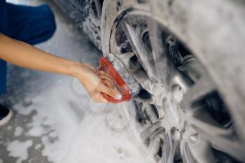 Female washer with brush in hand cleans wheel in foam, car wash. Woman washes vehicle, carwash station, car wash business