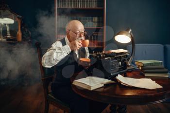 Elderly writer drinks coffee at vintage typewriter in his home office. Old man in glasses writes literature novel in room with smoke, inspiration