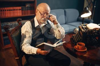 Elderly writer reads his work at vintage typewriter in home office. Old man in glasses writes literature novel in room with smoke, inspiration