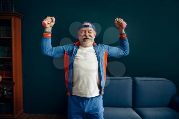 Elderly sportsman in uniform doing exercise with dumbbells at home. Adult male person on fitness training indoors, healthy lifestyle