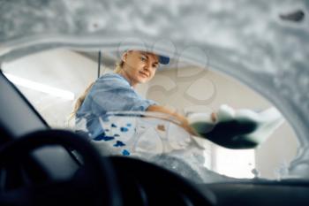 Female washer with sponge wipes the automobile windshield, view from interior, car wash. Woman cleans vehicle, carwash station, car-wash business