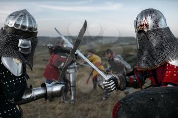 Medieval knights in armour and helmets fight with swords. Armored ancient warriors posing in the meadow