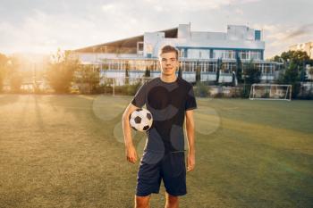 Male soccer player poses with ball in hands on the field at sunrise. Footballer on outdoor stadium, workout before game, football training