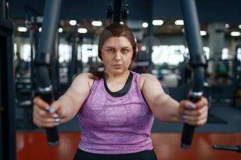 Overweight woman on exercise machine in gym, top view, active training. Female person struggles with excess weight, aerobic workout against obesity