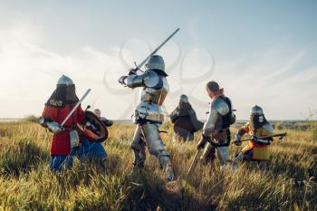Medieval knights in armor and helmets fight with sword and axe, great combat. Armored ancient warrior in armour posing in the field
