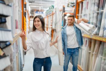 Young couple buying wallpapers in hardware store. Male and female customers look at the goods in diy shop