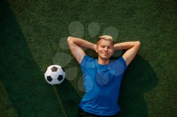 Male soccer player with ball lying on the grass on the field, top view. Footballer on outdoor stadium, workout before game, football training