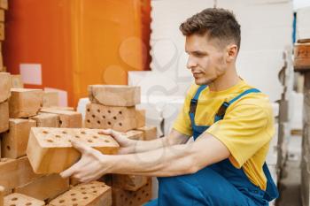 Male builder choosing bricks in hardware store. Constructor in uniform look at the goods in diy shop